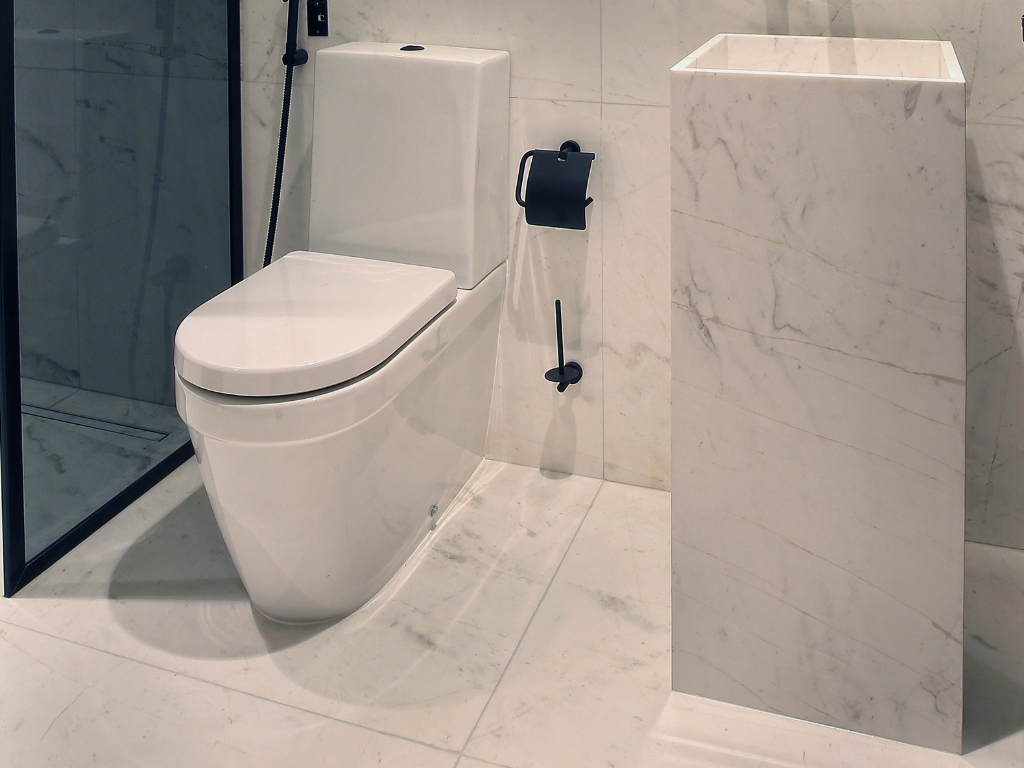 Toilet room corner image with marble bath furniture and white marble tiles with light veins on the floor and wall surface