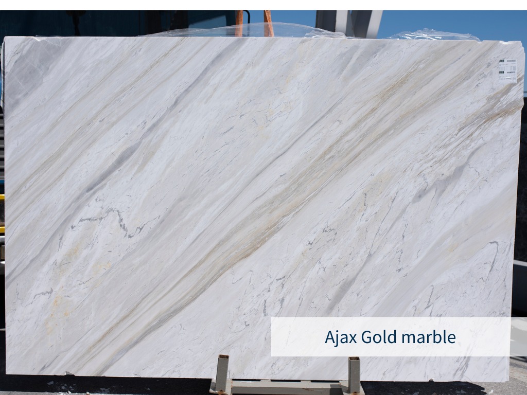 Slab of the white Greek marble Ajax with gold, gray, brown and blue diagonal veins, placed in an outdoor warehouse of a natural stone supplier